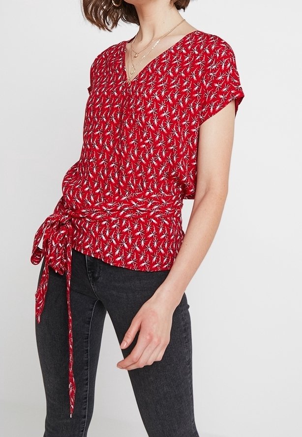 Červený top s krátkými rukávy a výstřihem do V, s květinovým vzorem, uvázaným pasem a volným střihem. Vyrobeno z lehké, texturované tkaniny.