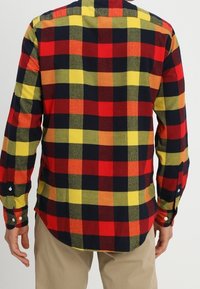 Camicia di flanella a maniche lunghe con un grande motivo a quadri rosso, giallo e blu navy. Realizzata in tessuto leggero con bottoni sui polsini.