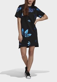 Svart kortärmad klänning med stora blå och lila blommönster och ränder, tillverkad av mjukt material, kombinerad med svarta sneakers.