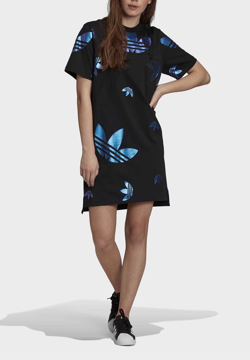 Svart kortärmad klänning med stora blå och lila blommönster och ränder, tillverkad av mjukt material, kombinerad med svarta sneakers.