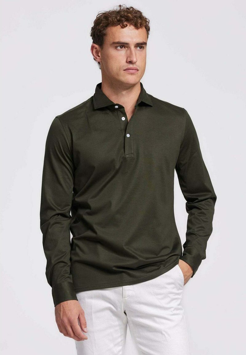 Donkergroene poloshirt met lange mouwen en kraag, met een drie-knoops sluiting en een gladde textuur. Gecombineerd met witte broek voor contrast.