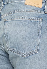 Jasnoniebieskie dżinsy o lekko wyblakłej strukturze, z tylną kieszenią i skórzaną metką marki na pasku.