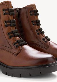 Brązowe skórzane botki za kostkę o gładkim wykończeniu, z metalowym zamkiem, materiałowymi sznurowadłami oraz solidną czarną podeszwą z głębokim bieżnikiem dla lepszej przyczepności.