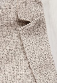 Beige strukturierter Stoff mit einem gewebten Muster aus sich kreuzenden Fäden, das eine subtile Oberflächenvariation und eine neutrale Farbgestaltung zeigt.