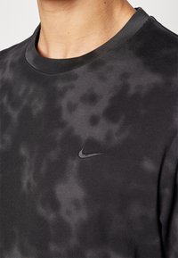 Black Nike t-shirt featuring a round neck, soft cotton fabric, subtle grey tie-dye pattern, and embroidered black logo on the left chest.
