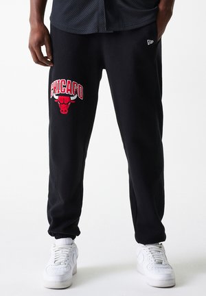Black sweatpants with an embroidered red "Chicago" logo and bull graphic, featuring a tapered fit and elastic ankle cuffs, paired with white sneakers.