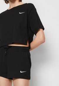 Woman wearing a black ribbed Nike short-sleeve crop top and matching drawstring shorts with white Nike logos.