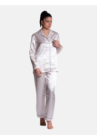 Completo di pigiama in raso di colore bianco sporco con piping nero. La maglia a maniche lunghe presenta bottoni; i pantaloni sono a gamba dritta e dal taglio comodo.