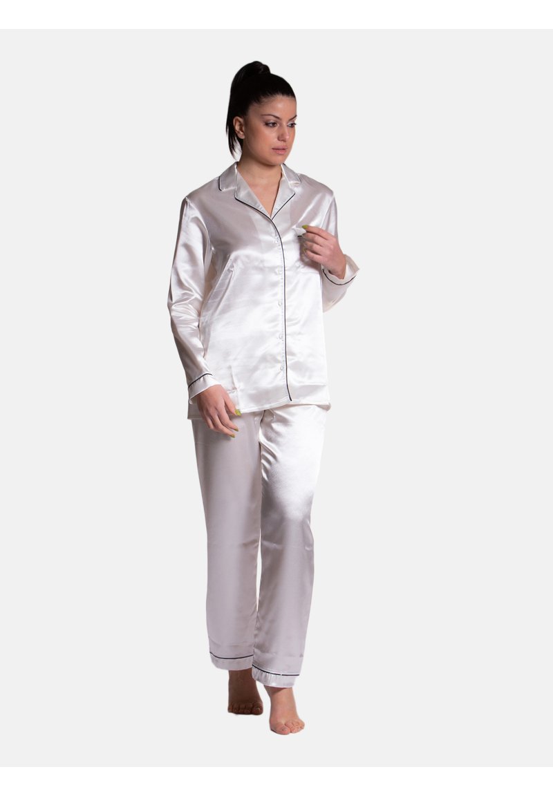 Completo di pigiama in raso di colore bianco sporco con piping nero. La maglia a maniche lunghe presenta bottoni; i pantaloni sono a gamba dritta e dal taglio comodo.