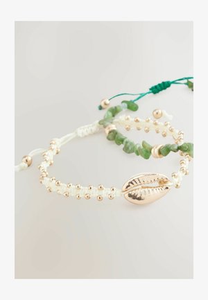 Bransoletki z koralików w kolorze zielonym, złotym i białym. Jedna z nich ma zawieszkę w kształcie złotej muszli; druga zawiera kamienie przypominające jadeit oraz dekoracyjne złote koraliki.