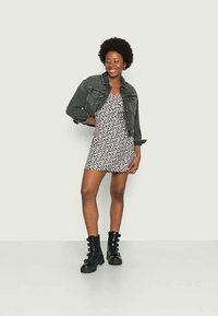 Jaqueta de ganga preta sobre um vestido de estampado floral nas tonalidades de branco, rosa e azul. Equipado com botas de combate pretas brilhantes com fivela.