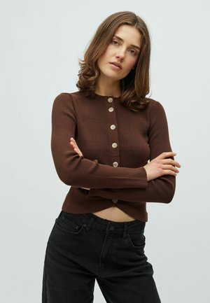 Brązowy prążkowany sweter rozpinany z okrągłym dekoltem, zapinany z przodu na guziki, o lekko skróconym kroju, w połączeniu z czarnymi dżinsami.