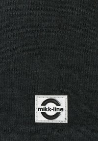 Mustan neulekankaan pinnassa on suorakulmainen valkoinen kenttä, jossa on ympyrälogo ja brändinimi "mikk-line" selvästi näkyvillä.