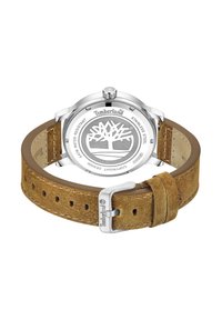 Brūns zamšs pulksteņa siksniņa ar sudraba nerūsējošā tērauda korpusu. Aizmugurē attēlots Timberland logo un ūdensizturības informācija. Minimālistisks dizains.