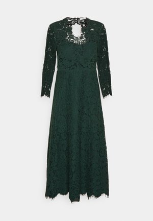 Tmavozelené čipkované šaty s dlhými rukávmi, s vysokým golierom a detailom v tvare kľúčovej diery, splývajúce do lemu so zúbkovaným okrajom.