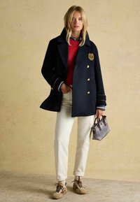 Tume sinise villasegu jope kuldsete nuppudega, kombineeritud punase sviitriga, valgete pükstega ja mustrilise käekotiga. Pruunid tenningid lõpetavad välimuse.