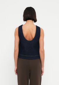 Σκούρο τζιν αμάνικο τοπ με χαμηλή πλάτη, που διαθέτει εφαρμοστή γραμμή και αντίθετη ραφή κατά μήκος του ποδόγυρου.