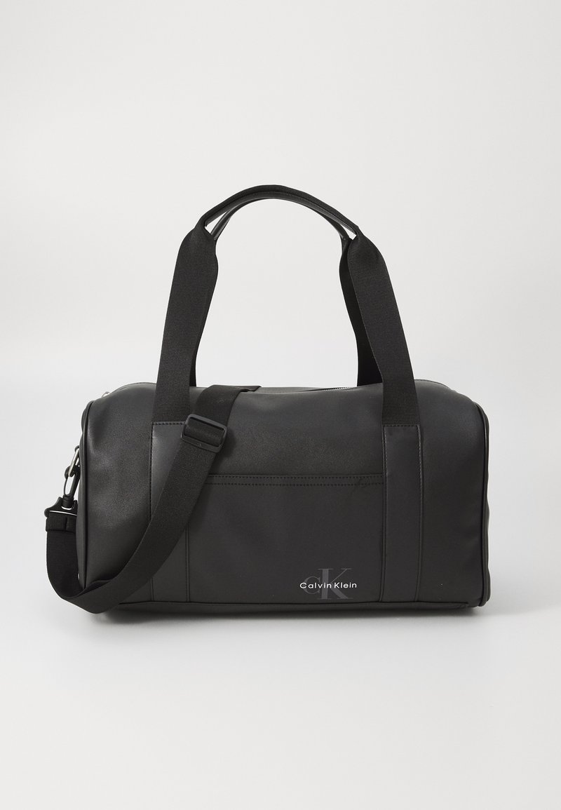 Schwarze Reisetasche aus glattem Material mit doppelten Griffen, verstellbarem Schultergurt und Fronttasche. Verfügt über ein dezentes Calvin Klein-Logo.