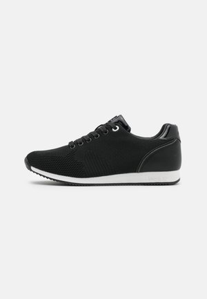 Czarny sneaker wykonany z dzianiny i skóry syntetycznej, z białą podeszwą, zaokrąglonym noskiem i sześcioma dziurkami na sznurowadła.