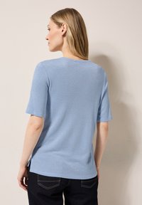 Svetle modré tričko s krátkým rukávem, s jemným leskem, kulatým výstřihem a bočními rozparky, vyrobené z měkké a hladké látky.