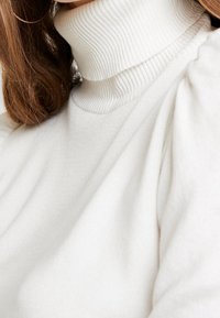 Weißer Rollkragenpullover mit gerippter Textur, puffigen Ärmeln und einem weichen, glatten Erscheinungsbild.