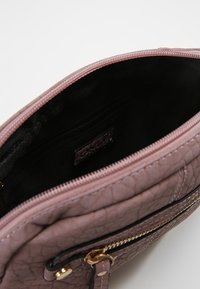 Vaaleanpunainen keinonahkainen laukku, jossa on teksturoitu pinta, kultaiset metalliosat, ylävetoketjullinen suljenta ja musta kangasvuori, jossa pieni vetoketjutasku.