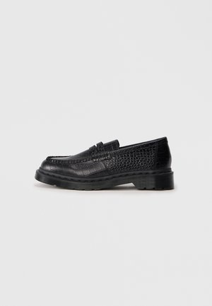 Mocassin en cuir noir avec motif crocodile texturé et semelle épaisse en caoutchouc sur fond gris clair uni.