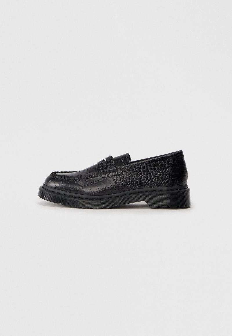 Mocassin en cuir noir avec motif crocodile texturé et semelle épaisse en caoutchouc sur fond gris clair uni.