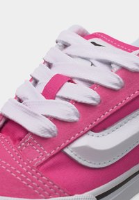 Κοντινό πλάνο ροζ αθλητικού παπουτσιού με λευκά κορδόνια και λευκή κυματιστή λεπτομέρεια στο πλάι.