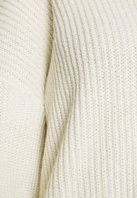 Gros plan sur un tissu tricoté de couleur crème avec une texture côtelée verticale et des détails de fil doux et tissé.