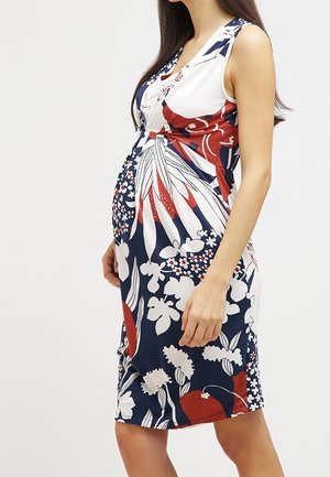 Pregnant woman wearing a sleeveless, knee-length dress with a red, white, and navy blue floral pattern, standing in profile.
