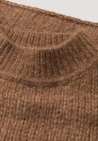 Brauner gestrickter Pullover mit hohem Rippkragen und strukturiertem, weichem Garn mit variierenden Maschen, das Wärme und Gemütlichkeit betont.