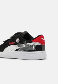 Baskets Puma noir et blanc avec talon rouge, bandes Velcro, et un panthère de dessin animé jouant au football sur le côté près de la bande blanche Puma.