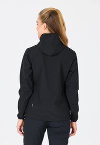 Veste softshell noire avec capuche, design ajusté, poignets élastiques et lignes épurées, mettant en valeur une texture lisse et un minimum de détails.