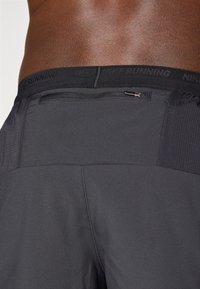 Czarne spodenki biegowe z teksturowanym materiałem, elastycznym pasem w talii z logo "NIKE RUNNING" oraz małą kieszonką na zamek z tyłu.