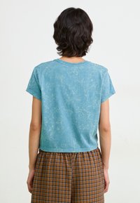 Kortärmad, croppad t-shirt i ljusblått med en tvättad textur. Kombinerad med bruna rutiga shorts.