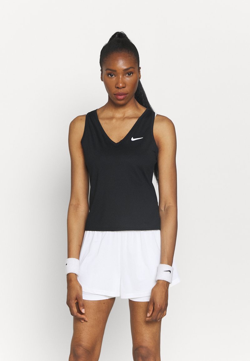Top deportivo negro sin mangas con escote en V, presenta un logo de Nike en blanco. Combinado con pantalones cortos blancos y pulseras blancas. Textura de tela suave.