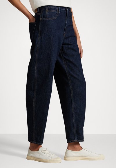 Mörkblå denimjeans med lös passform, hög midja och framträdande sid sömmar. Kombineras med vita canvassneakers.