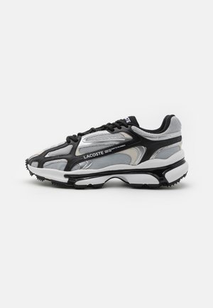 Czarny, biały i szary sneaker Lacoste z siateczkowymi panelami, grubą amortyzowaną podeszwą, czarnymi sznurówkami i błyszczącymi srebrnymi akcentami z boku.