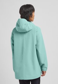 Veste imperméable vert menthe avec capuche, dotée d'une coupe droite, de poignets élastiqués et d'un design minimaliste.