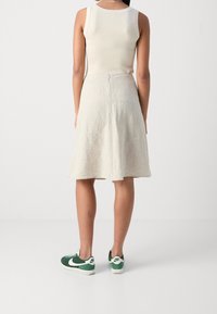 Falda midi de lino beige con forma en A, combinada con zapatillas Nike verdes y blancas, que muestra una textura suave y un diseño minimalista.
