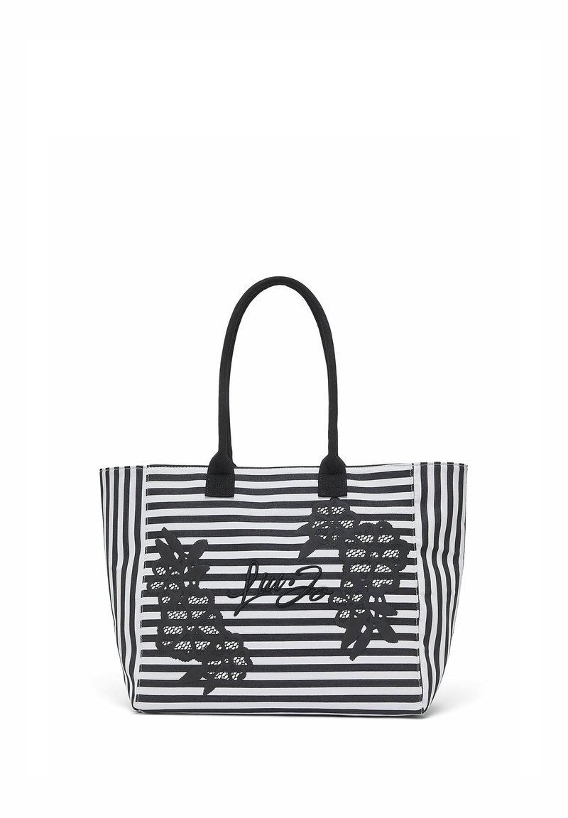 Sac fourre-tout à rayures noires et blanches avec poignées noires, appliques de dentelle florale et logo en écriture cursive au centre avant.