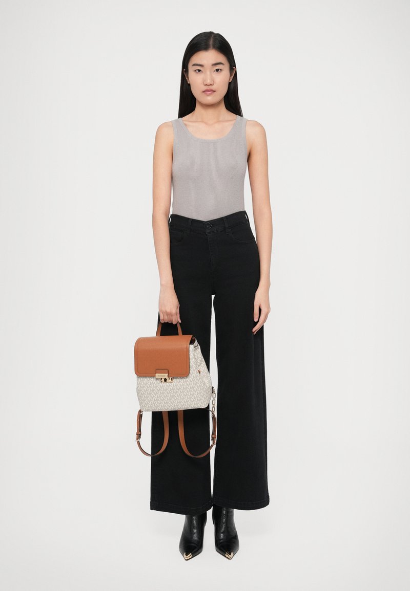 Szary prążkowany top na ramiączkach, czarne szerokie spodnie, czarne botki z ostrym noskiem. Plecak w kolorze brązowo-kremowym z wzorem, z klapą na górze i złotymi elementami metalowymi.