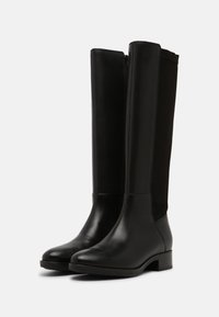 Botas negras hasta la rodilla, hechas de cuero y tejido, con un acabado suave, punta redondeada, tacón bajo y cierre lateral con cremallera.