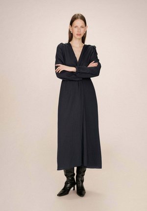 Robe longue navy avec un décolleté en V, des manches longues et une texture subtile. Associée à des bottes à talons noirs, sur un fond neutre.