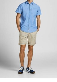 Light blue short-sleeve button-up shirt, beige shorts, and black sneakers with blue and white accents. Shirt features a chest pocket.