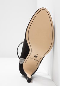 Chaussure à talon haut en daim noir avec un bout pointu, dotée d'une fine bride grise et d'une semelle en caoutchouc beige. Taille 37 indiquée sur la semelle.