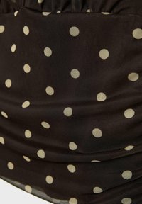 Czarna tkanina z równomiernie rozmieszczonymi białymi groszkami i delikatnymi marszczeniami tworzącymi miękkie fałdy.