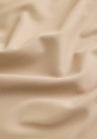 Világos bézs színű, sima, enyhén fénylő textil, amely lágy, folydogáló redőkkel és finom árnyalatokkal rendelkezik.