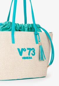 Borsa a spalla intrecciata beige con dettagli turchesi, caratterizzata da una parte superiore arricciata, dettagli in frange e logo ricamato "V°73 VENEZIA".